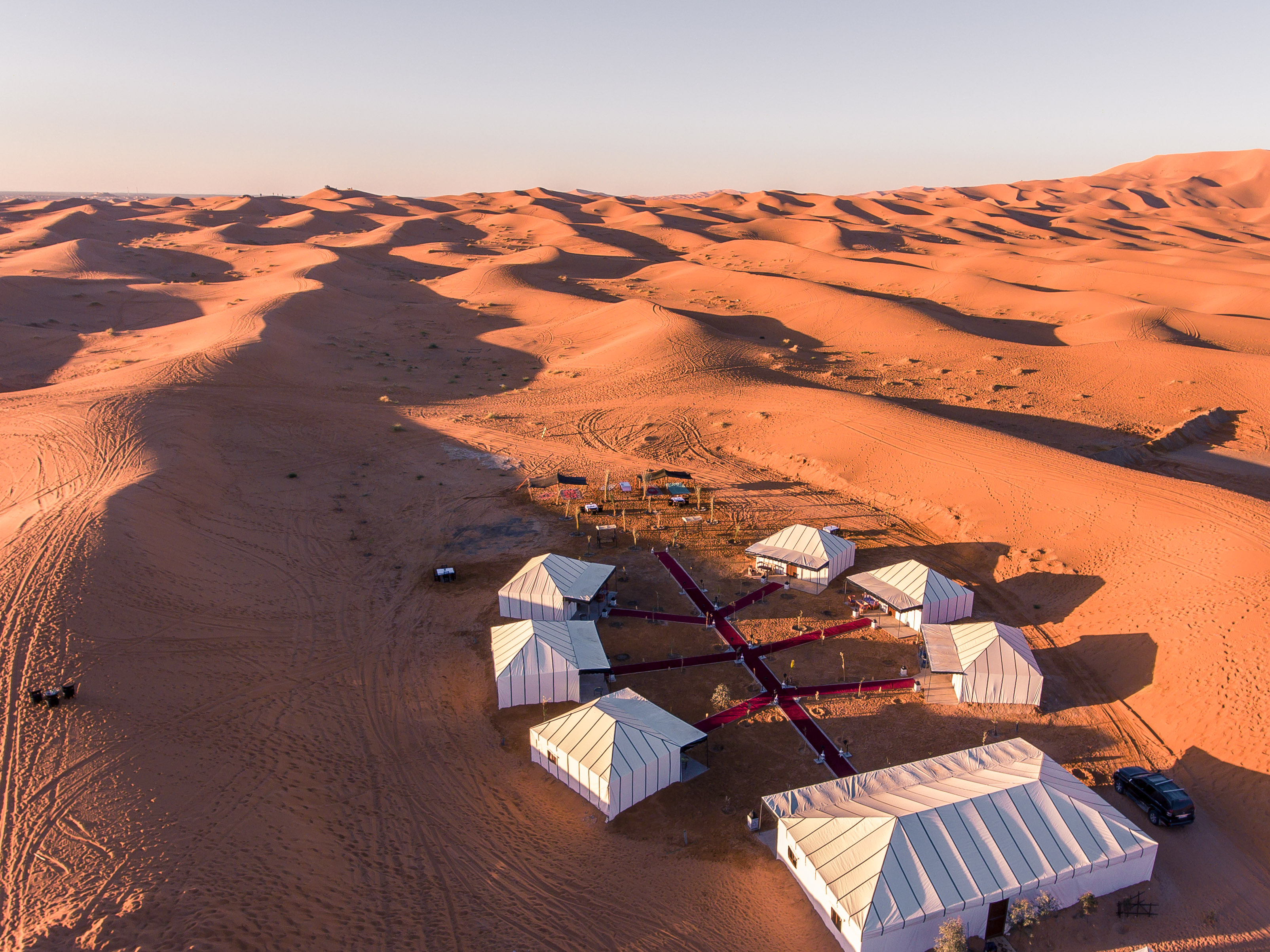 Aerial view of luxury Merzouga desert camp setup with elegant white tents and Moroccan lanterns